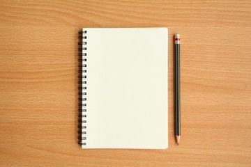 Top view of blank page notebook with pencil on wood background.