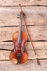 Violin and fiddle stick on wooden planks. Vintage violin and bow on old wooden boards, top view.
