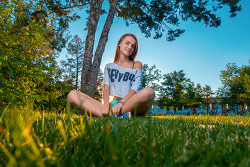 Ginger haired girl sitting on grass cross legged and looking in camera with cute smile on her face, copyspace on grass