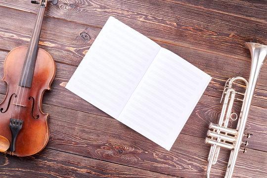 Old violin, trumpet and musical notes. Symphonic music instruments on wooden background. Orchestra music classic instruments. Lesson of classical music.
