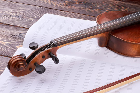 Close up violin and musical notes. Brown violin scroll and peg box on music notes. Retro instrument of classical music.