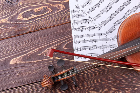 Violin, fiddle stick and musical notes. Old violin on textured wooden background, cropped image. Detail of violin.