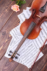 Musical composition on wooden backgoround. Violin, musical notes and rose on brown wooden table, top view.