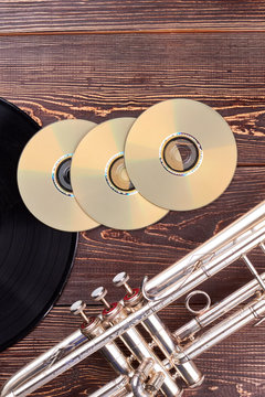 Blank cd discs and trumpet. Black vinyl record, dvd discs and trumpet on wooden surface, vertical image.