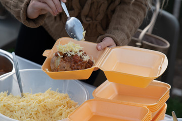 Jacket potato being served into a take away lunch box.