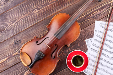 Fototapeta premium Musical background with classical equipment. Violin, musical score pages and blank mug on wooden background with copy space.