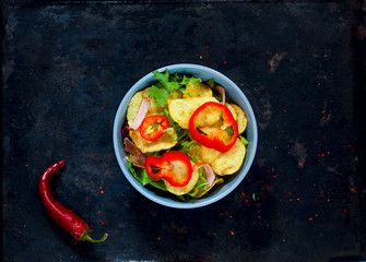 Potato Salad with Bacon, richly seasoned with select spices in a blue bowl on vintage rusty metal background.Top view, copy space, flat lay.