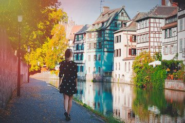 Fototapeta na wymiar Young style girl in black dress waking along the canal in Strasbourg, France. Autumn season time