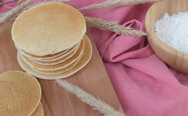 Delicious pancakes on a wooden board with ingredients and flowers