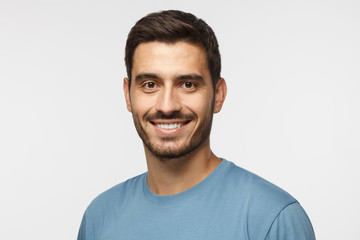 Headshot of young handsome european caucasian man isolated on gray background. wearing casual blue t-shirt, smiling happily and friendly at camera, looking confident and relaxed