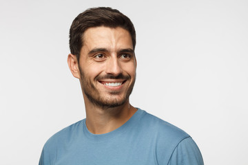 Close up portrait of smiling handsome male in blue t-shirt looking right, isolated on gray...