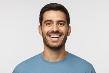 Close up horizontal shot of handsome smiling broadly unshaven young man in blue tshirt laughing out...