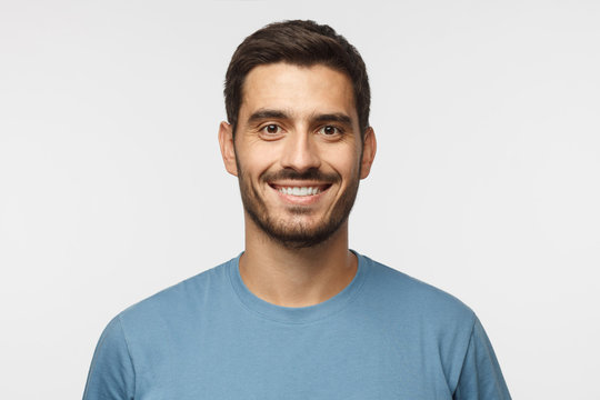 Close up portrait of young smiling handsome guy in blue t-shirt isolated on gray background