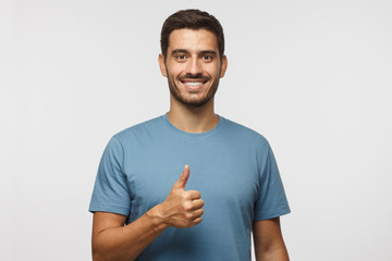 Young man isolated on grey background showing thumb up with positive emotions and happiness....