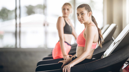 Fighting diet!Woman exercising on machine together.Attractive builder muscles women looking camera...