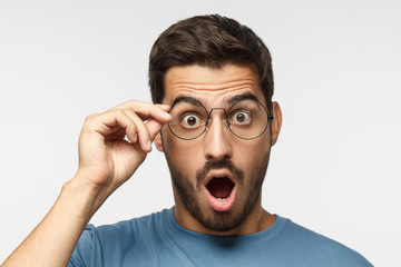 Young man in blue t-shirt shouting oh my god with open mouth, holding round glasses, surprised by low price and sales
