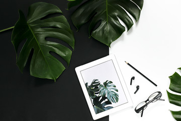 Office workspace layout with tablet accessories on white background, tropical monstera leaves