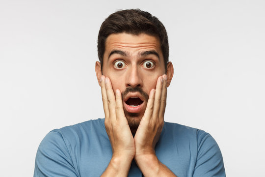 Young man isolated on grey background, dressed in casual clothes, with round eyes, experiencing deep astonishment and fear