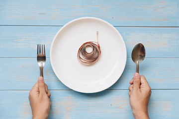 Top view Woman hand holding spoon and fork above white dish with pink Measuring tape on blue pastel...