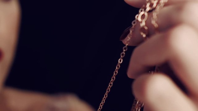 Close-up of  girl's hand with red nails holding gold chain. Jewelry for women. In the studio on a black background.