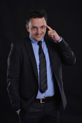 Portrait of a man smiling wearing a suite, blue shirt and a black tie isolated on black background.