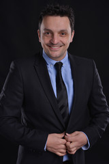 Portrait of a man smiling wearing a suite, blue shirt and a black tie isolated on black background.