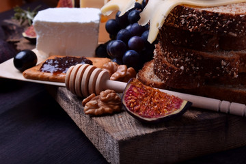 Assortment of appetizers: different sorts of cheese, crackers, grapes, nuts, olive marmalade, figs and olives against the dark background