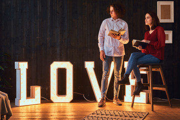 Young student couple reading together in a room decorated with voluminous letters with illumination.
