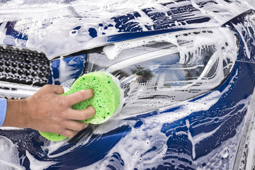 Man washing a soapy blue car with a green sponge.