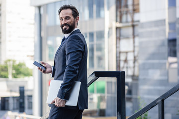 Joyful bearded businessman holding his laptop outdoors