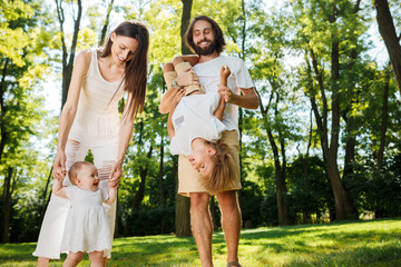 Fototapeta premium Happy family on the open air. Young dark-haired woman walking with her little daughter and her husband having fun with son.