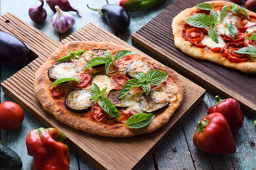 Vegetarian meal. Homemade pizzas with aubergines, bell peppers, tomatoes, mozarella and basil on oak boards served with raw ingredients