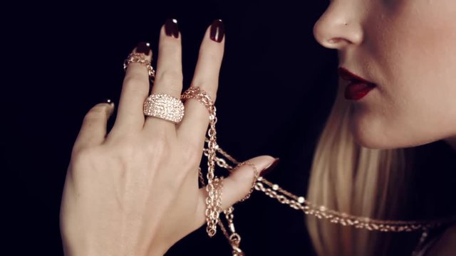 Close-up of  girl's hand with red nails holding gold chain. Jewelry for women. In the studio on a black background. Large gold ring with diamonds on finger.