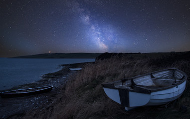 Vibrant Milky Way composite image over landscape of Old abandoned rowing boats on shore of lake