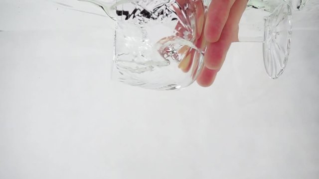 Tumbler is immersed in water, water fills glass, slow motion on white background