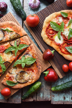 Vegetarian rustic pizzas. Freshly baked pizzas with aubergines, bell peppers and tomatoes on oak boards with raw vegetables