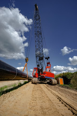 Pipelinebau - roter Kran hebt die Stahlleitung zur Verlegung im Erdboden an.