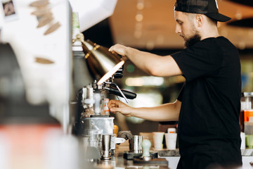 A stylish young man with beard,wearing casual clothes,cooks coffee in a coffee machine in a cozy...
