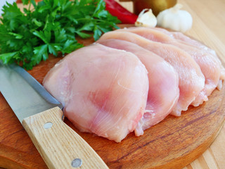 Sliced chicken breast with herbs and vegetables on wooden chopping board, closeup.