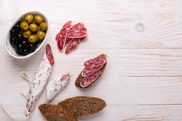 Salami and bread on white wooden background. Top view. Copy space