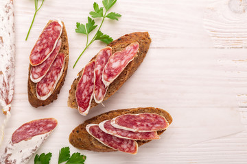 Salami and bread on white wooden background. Top view. Copy space