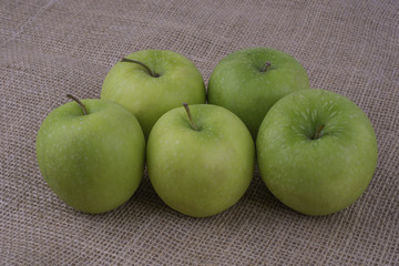 Five green granny smith apples on burlap surface. View from above.