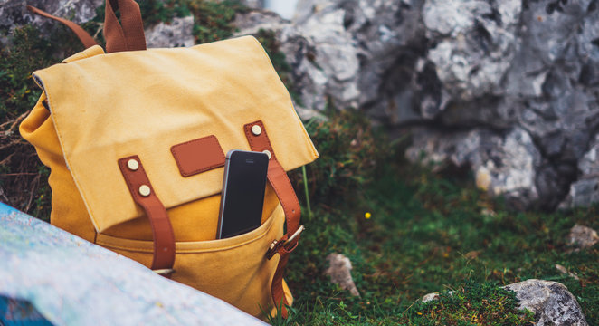 Hipster hiker tourist yellow backpack and mobile phone, map on background green grass nature in mountain, blurred panoramic landscape, traveler relax holiday concept, view wayroad in trip vacation