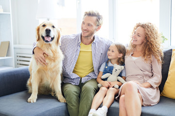Cheerful father, mother and little daughter looking at their purebred pet while enjoying home rest