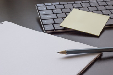 Pencil, notebook on a dark table, next to the keyboard