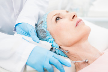 Gloved cosmetician holding two steel electric rods with small spheres on ends close to client neck