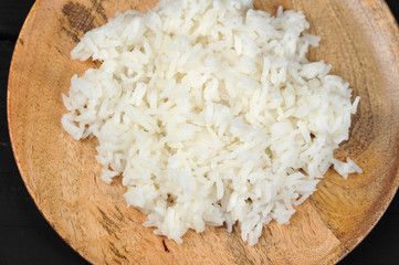 Boiled rice on a round wooden plate. View from above. Dark background. Close-up. Macro photography.