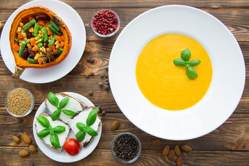 Pumpkin cream soup with basil leaves, baked pumpkin with vegetables: carrots, beans, haricot, bruschettas with cream cheese and tomatoes. Thanksgiving background. Autumn pumpkin spice.