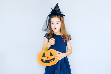 cheerful happy little girl with red horns and pumpkin stands on a gray background. selective focus.