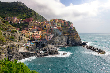 View of beautiful colorful traditional fisherman houses on a cliff over Ligurian sea on cloudy day in Manarola village, Cinque Terre national park, Liguria, La spezia province, Italy.